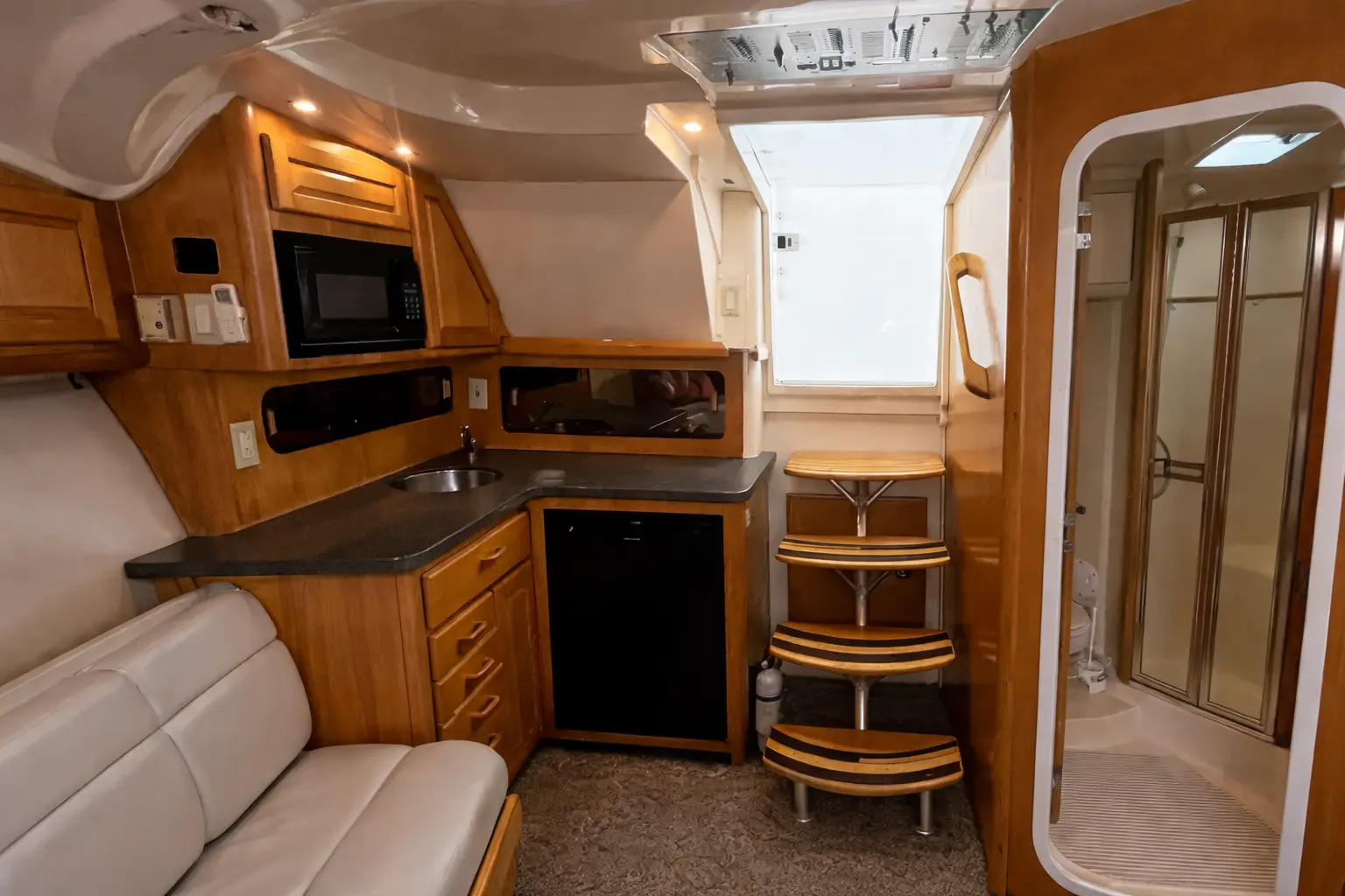 Wood-paneled cabin of a sportfishing boat with a galley, microwave, sofa and glass shower