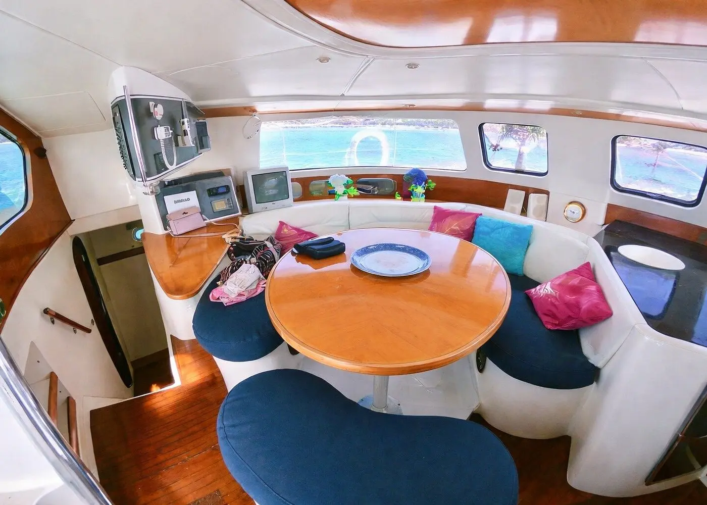 Catamaran saloon with a round wooden table, navy seating and pink and teal cushions