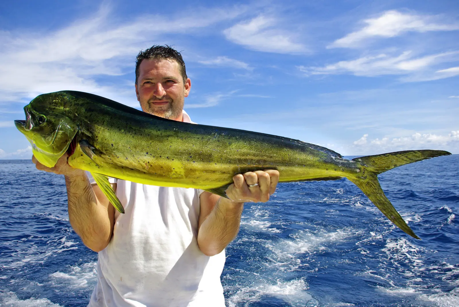 Smiling angler holding a mahi-mahi aboard with the blue Pacific off Costa Rica behind