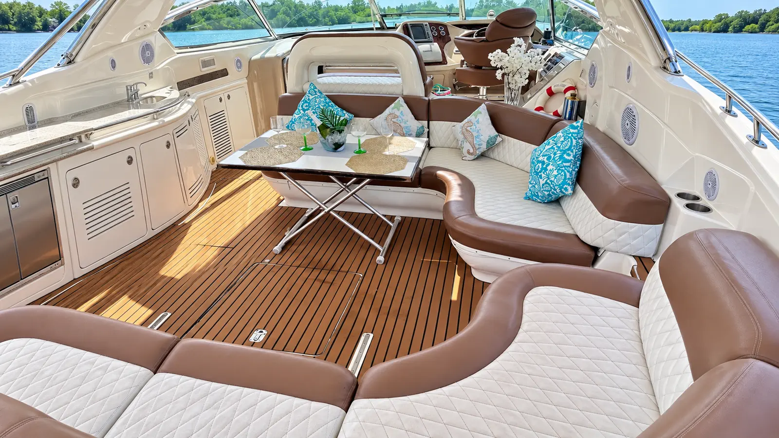Cockpit lounge of a motor yacht with brown and white quilted seating, turquoise pillows and teak floor