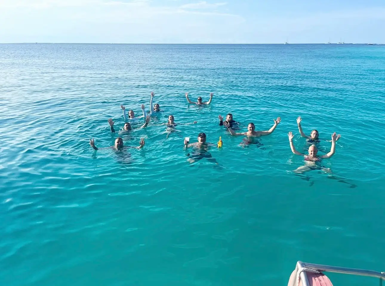 Group of guests swimming and waving in open turquoise water beside the catamaran off Zanzibar