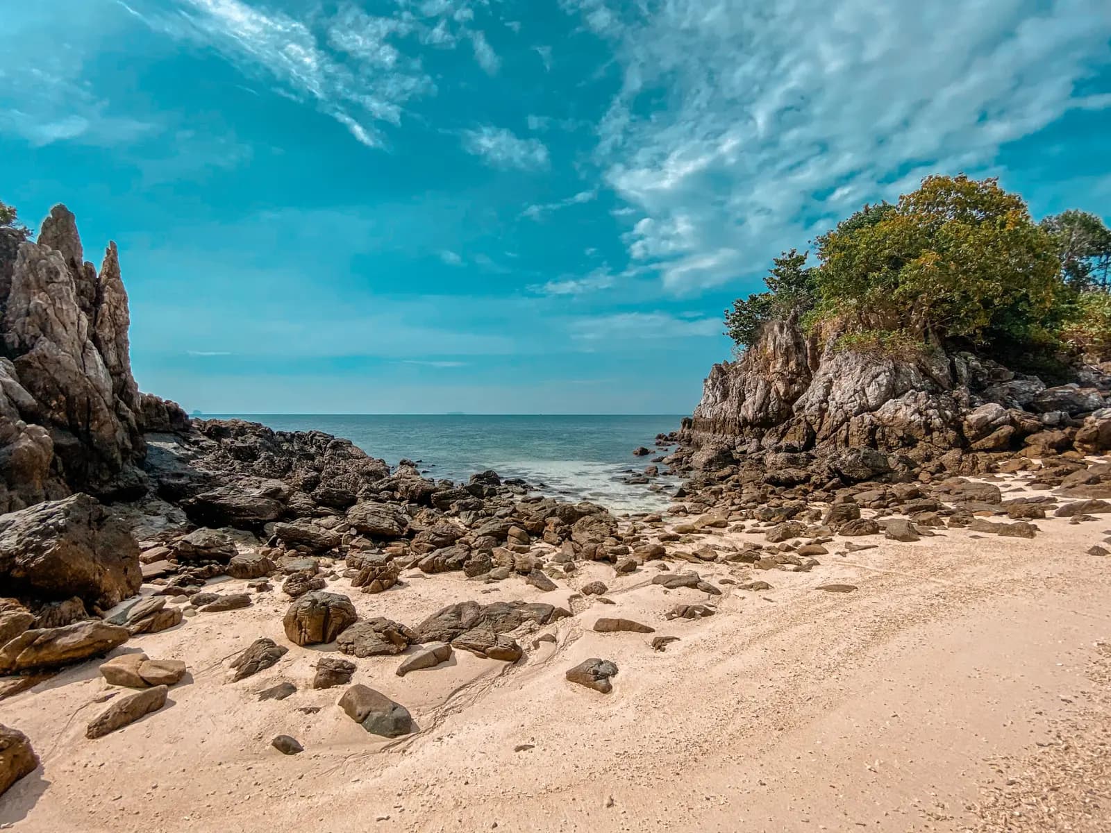Sandy cove scattered with boulders, opening to the sea between rocky outcrops on a Khai island