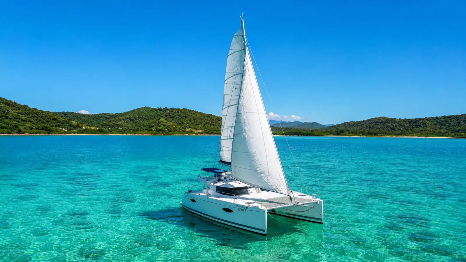 Sailing catamaran under mainsail on shallow turquoise water near a green island in Papagayo