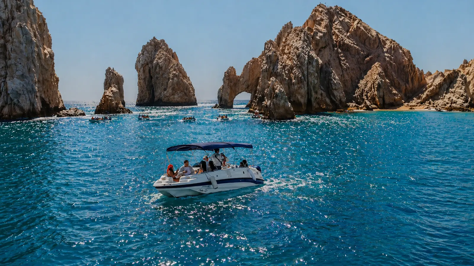 Small yacht with a canopy cruising toward the Arch of Cabo San Lucas and its rock spires