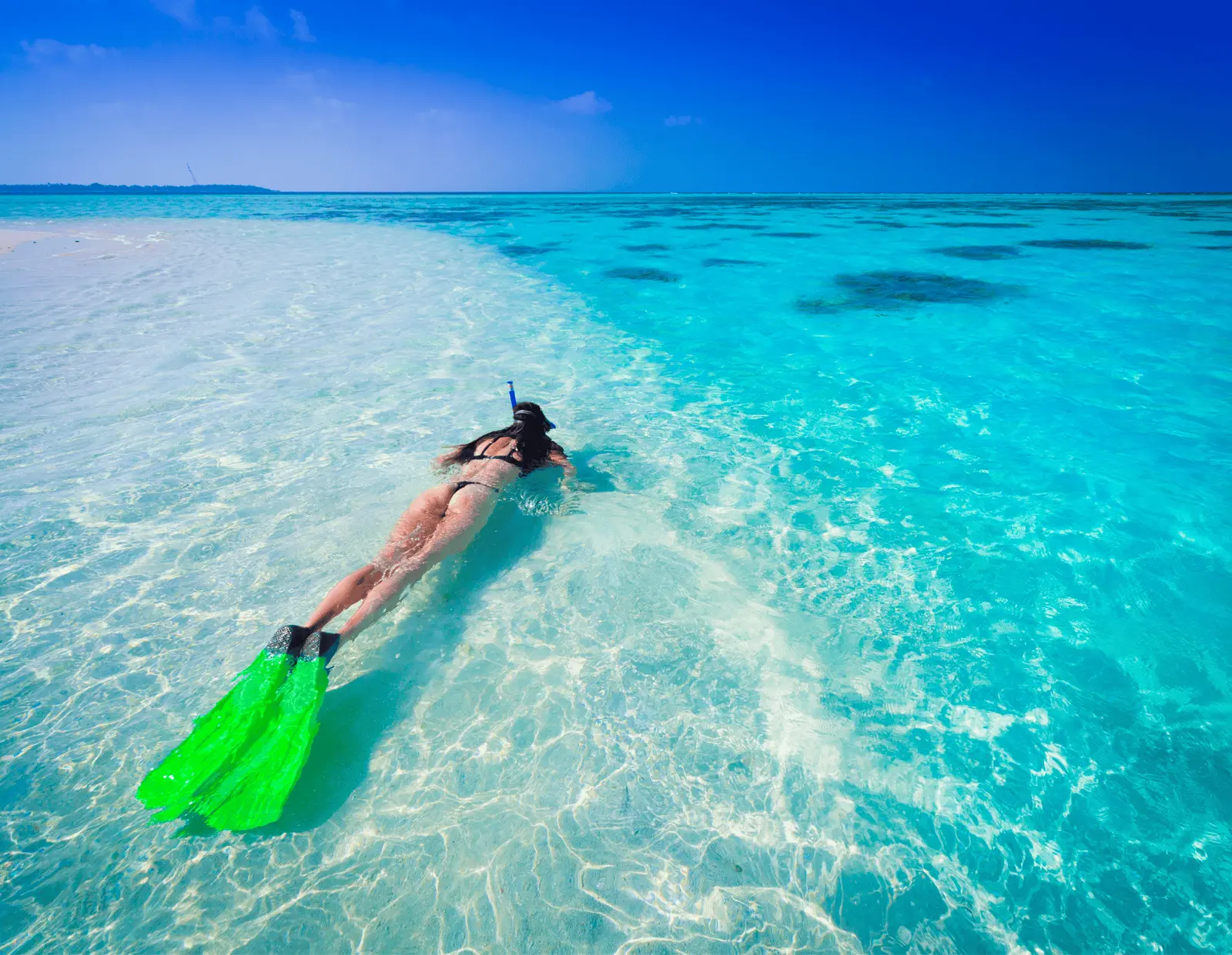 Snorkeler with green fins swimming over a pale sandbar in clear shallow water off Zanzibar