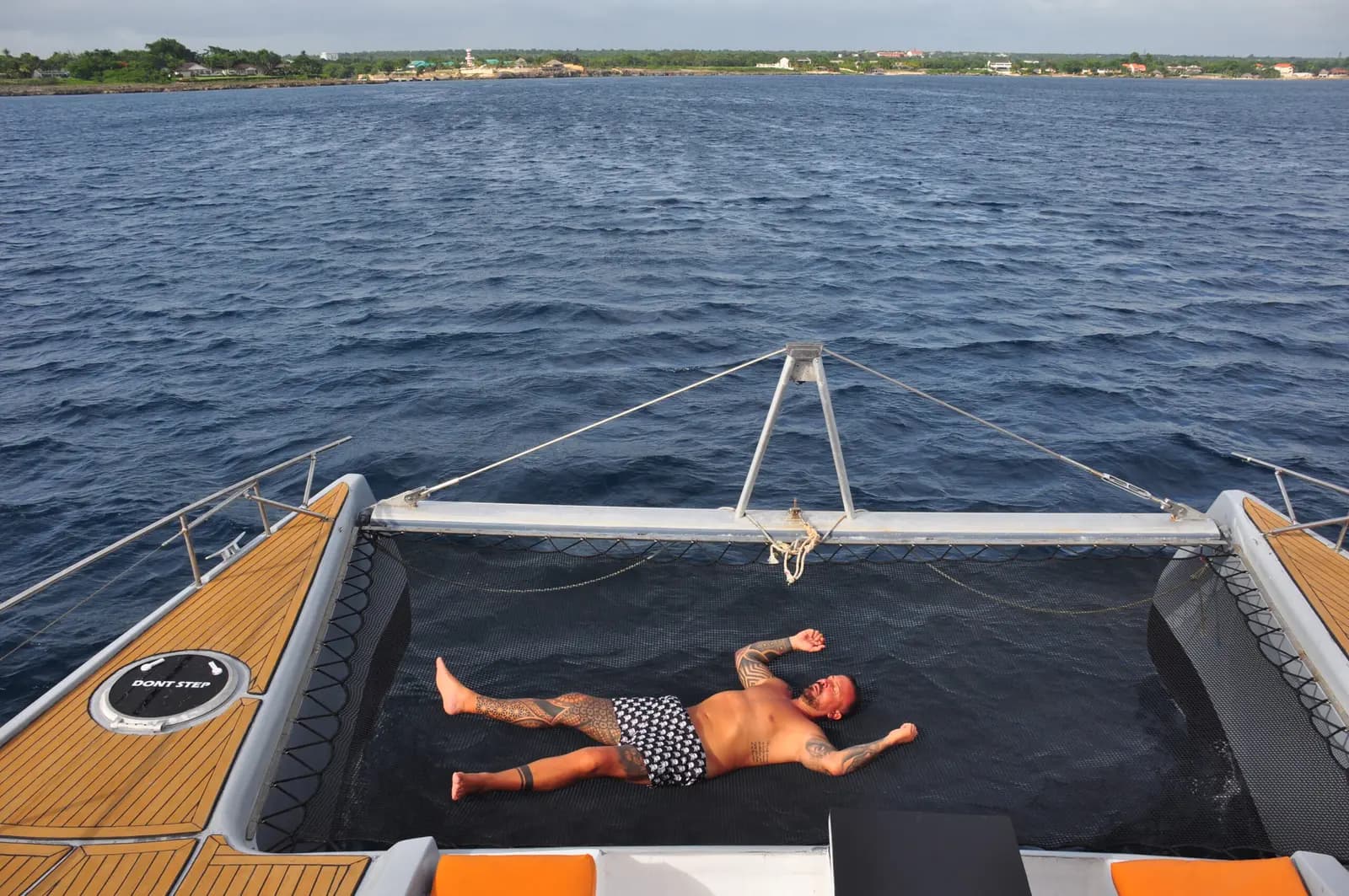 Man stretched out on the bow trampoline of a power catamaran cruising deep blue water off Punta Cana