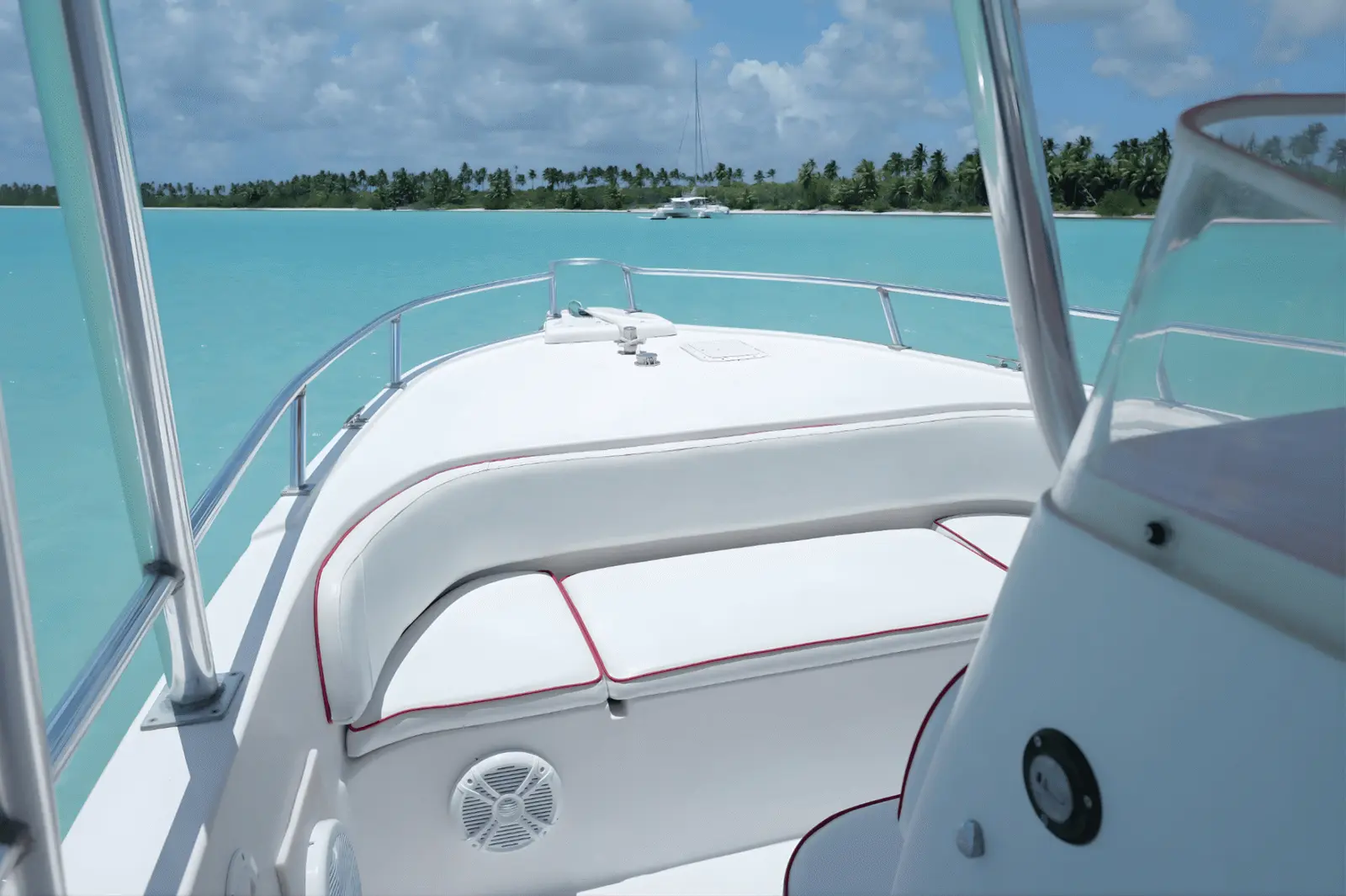 Cushioned bow seat of a speedboat looking toward a catamaran anchored off palm-lined Saona Island