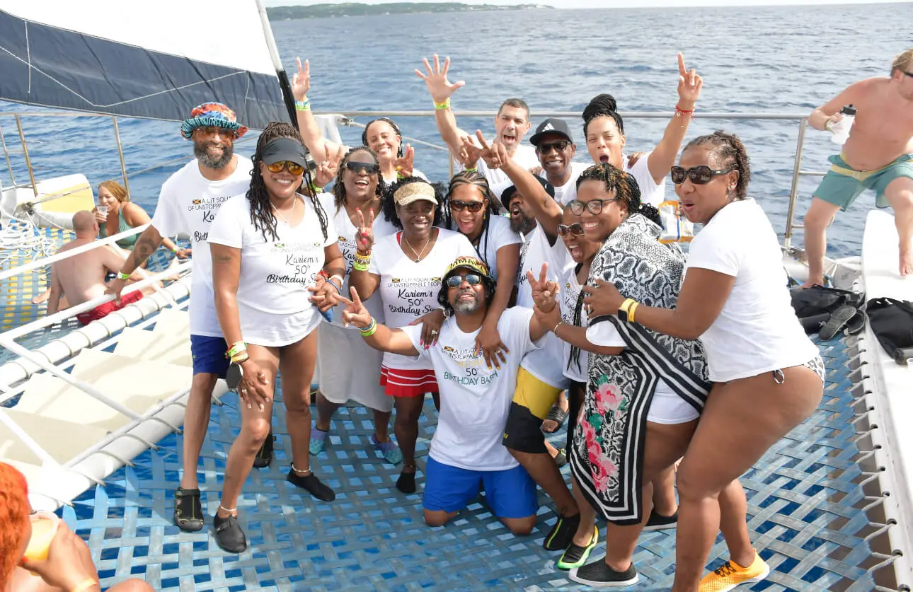 Group in matching white T-shirts cheering on a catamaran's trampoline net on the open sea