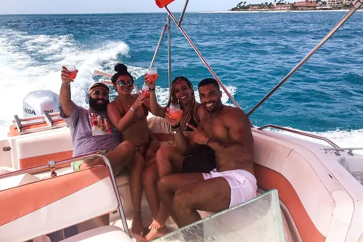 Four guests raising drinks on a speedboat cutting across the water off Aruba