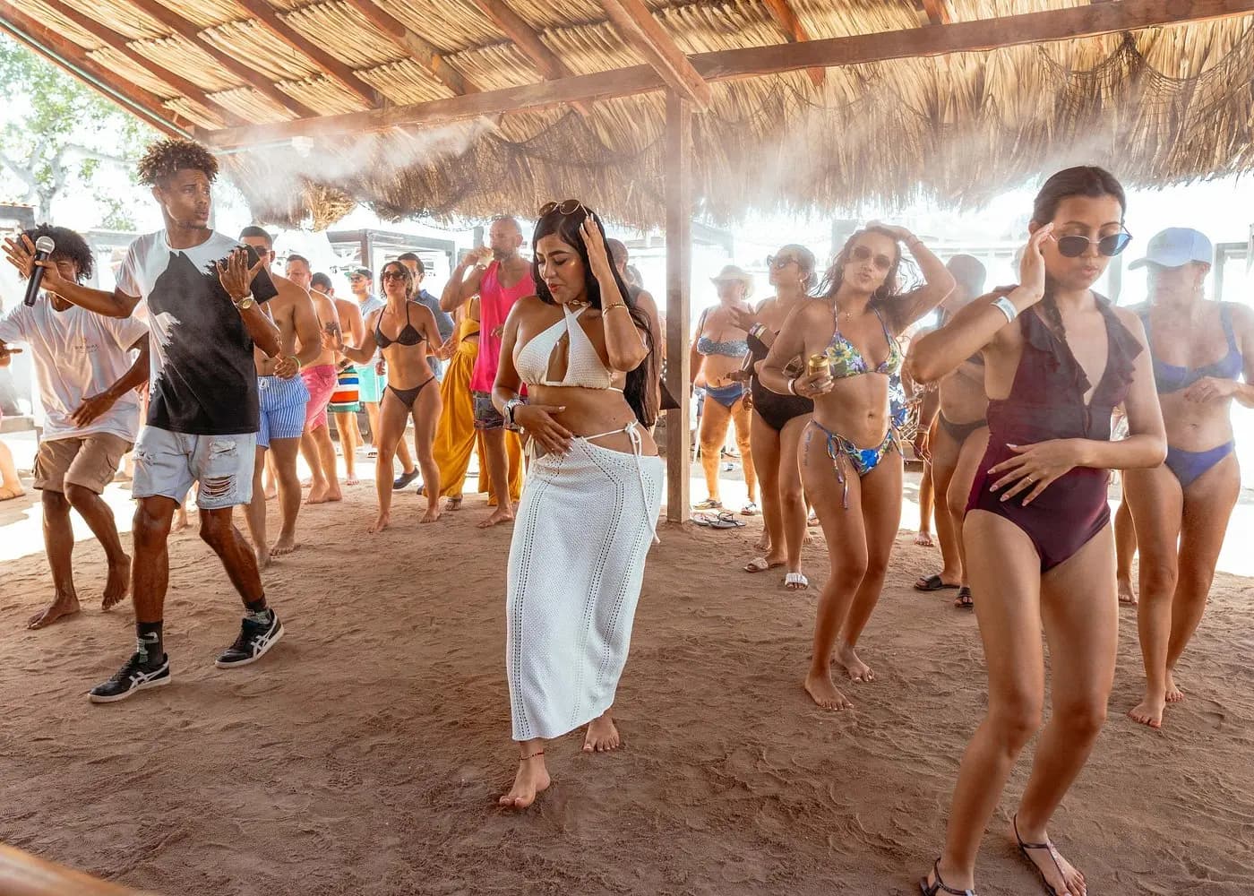 Guests in swimwear dancing together on the sand under the thatched roof of a Rosario Islands beach club