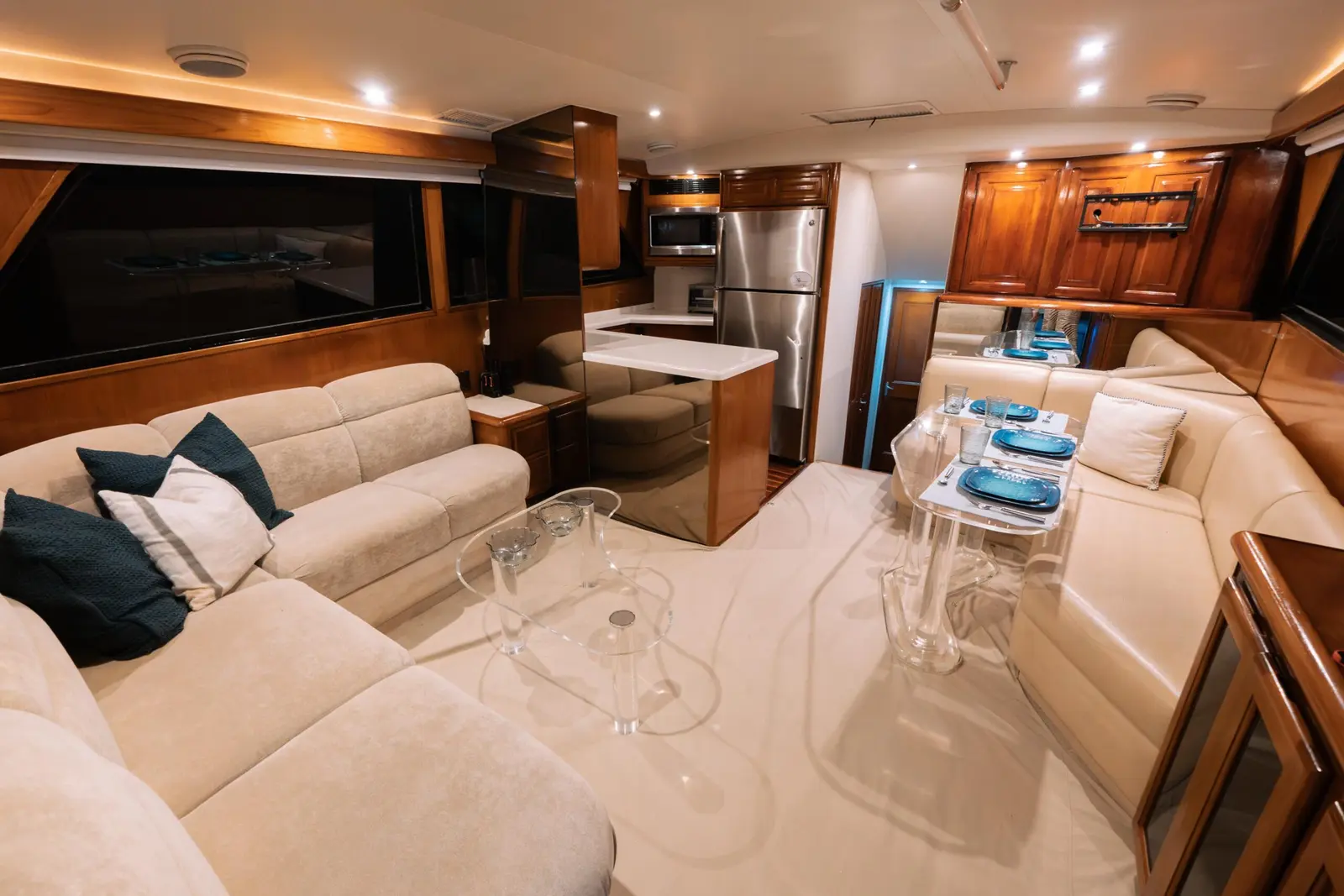 Yacht salon with cream sofas, a glass coffee table and a wood-trimmed galley with a steel fridge