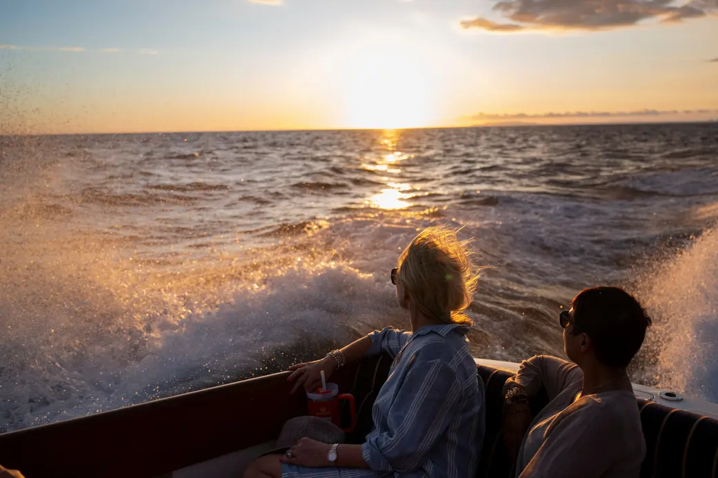Couple sitting at the stern of a yacht watching the sunset over a spray-filled wake off Costa Rica