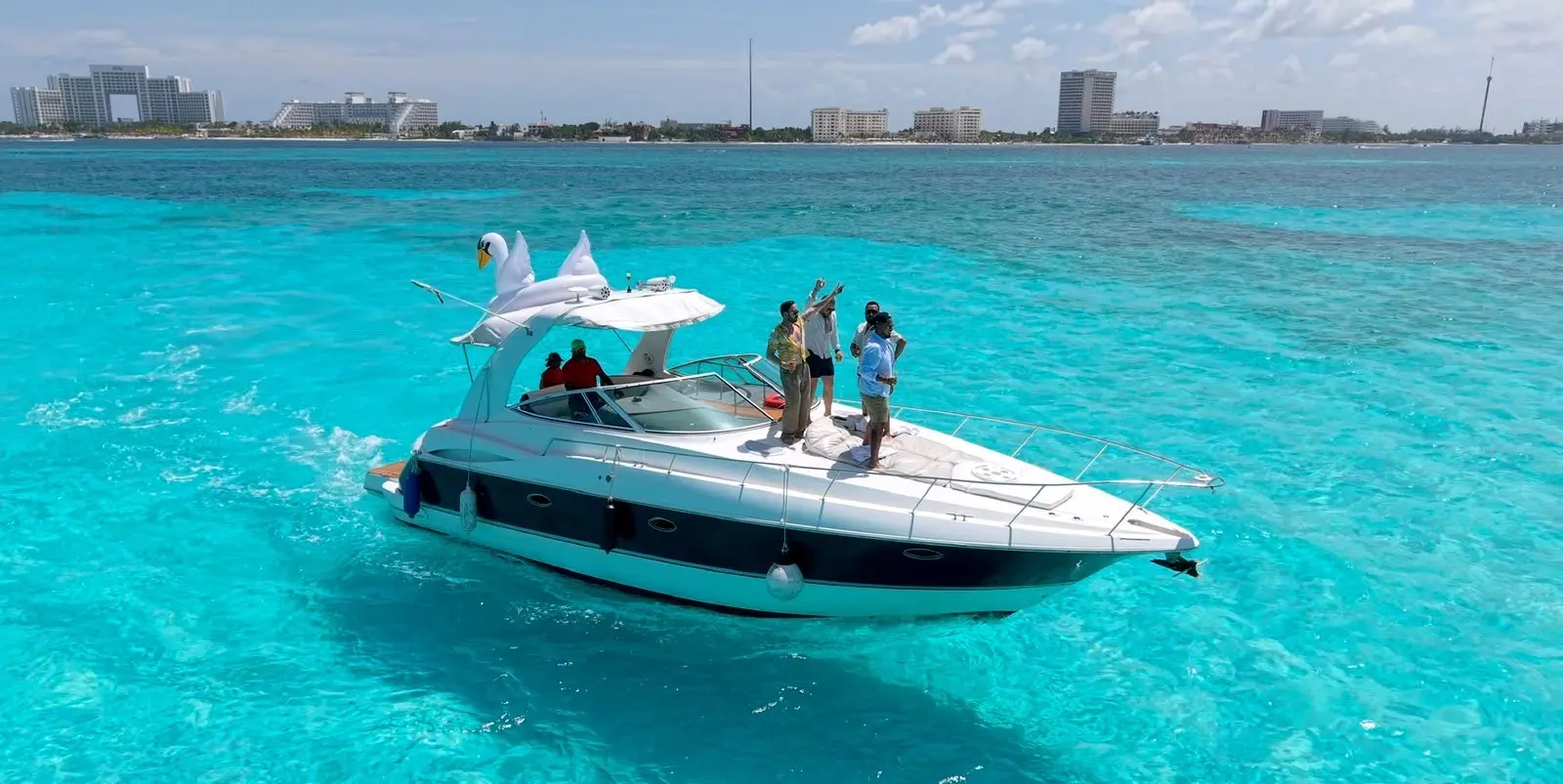 Guests on the bow of an express cruiser anchored in turquoise water with the Cancún skyline behind