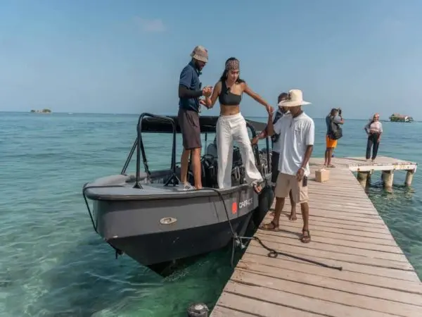 Woman in white stepping from a speedboat onto a wooden pier with crew help in the Rosario Islands