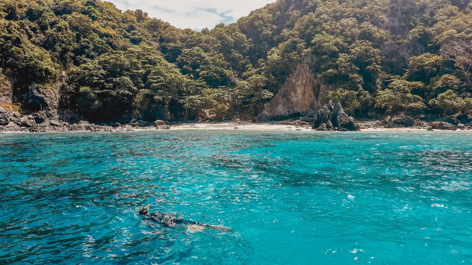 Turquoise lagoon ringed by jungle-covered cliffs and a narrow beach in Phang Nga Bay