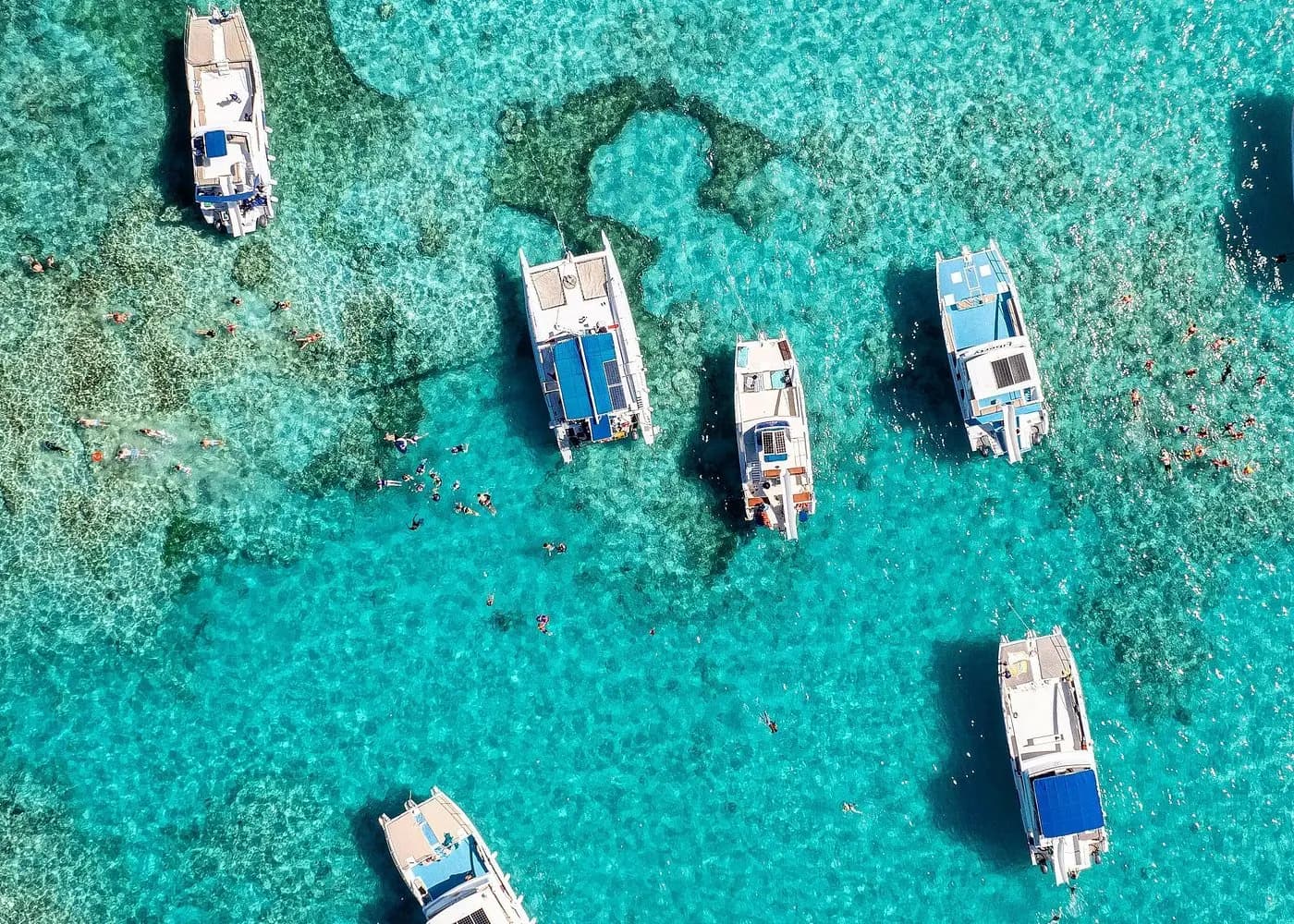 Top-down view of catamarans anchored over a turquoise reef off Punta Cana, snorkelers between them