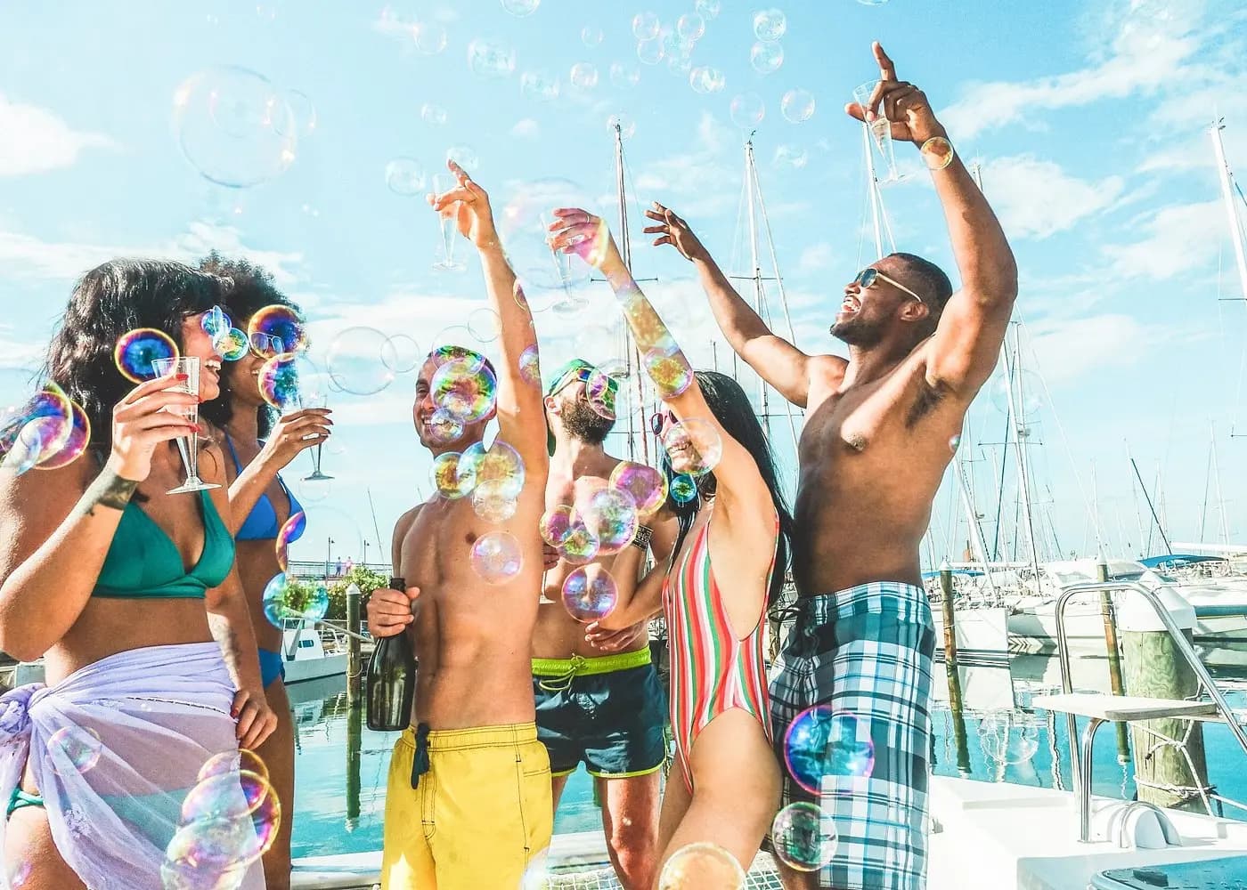 Friends raising drinks and arms amid floating soap bubbles on a boat docked in a Samaná marina