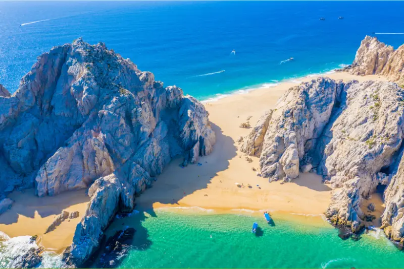 Aerial view of Lover's Beach, a strip of sand between granite cliffs with small boats in turquoise water