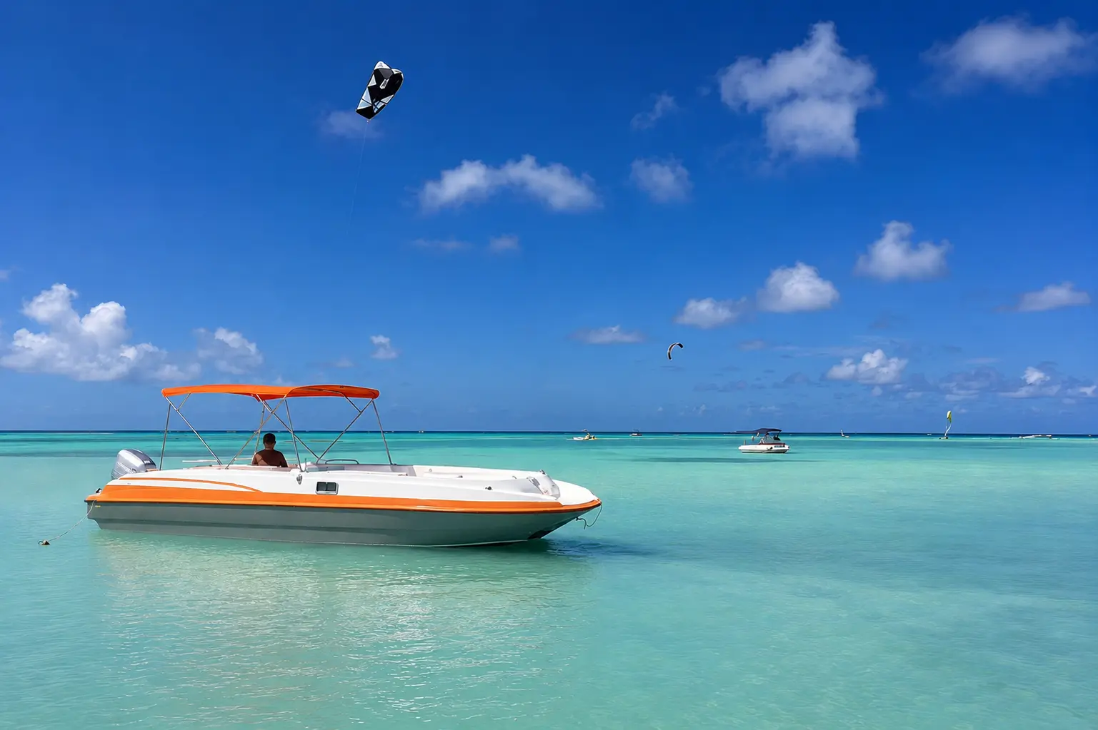 Deck boat with an orange canopy anchored in shallow turquoise water off Aruba as a kite flies above