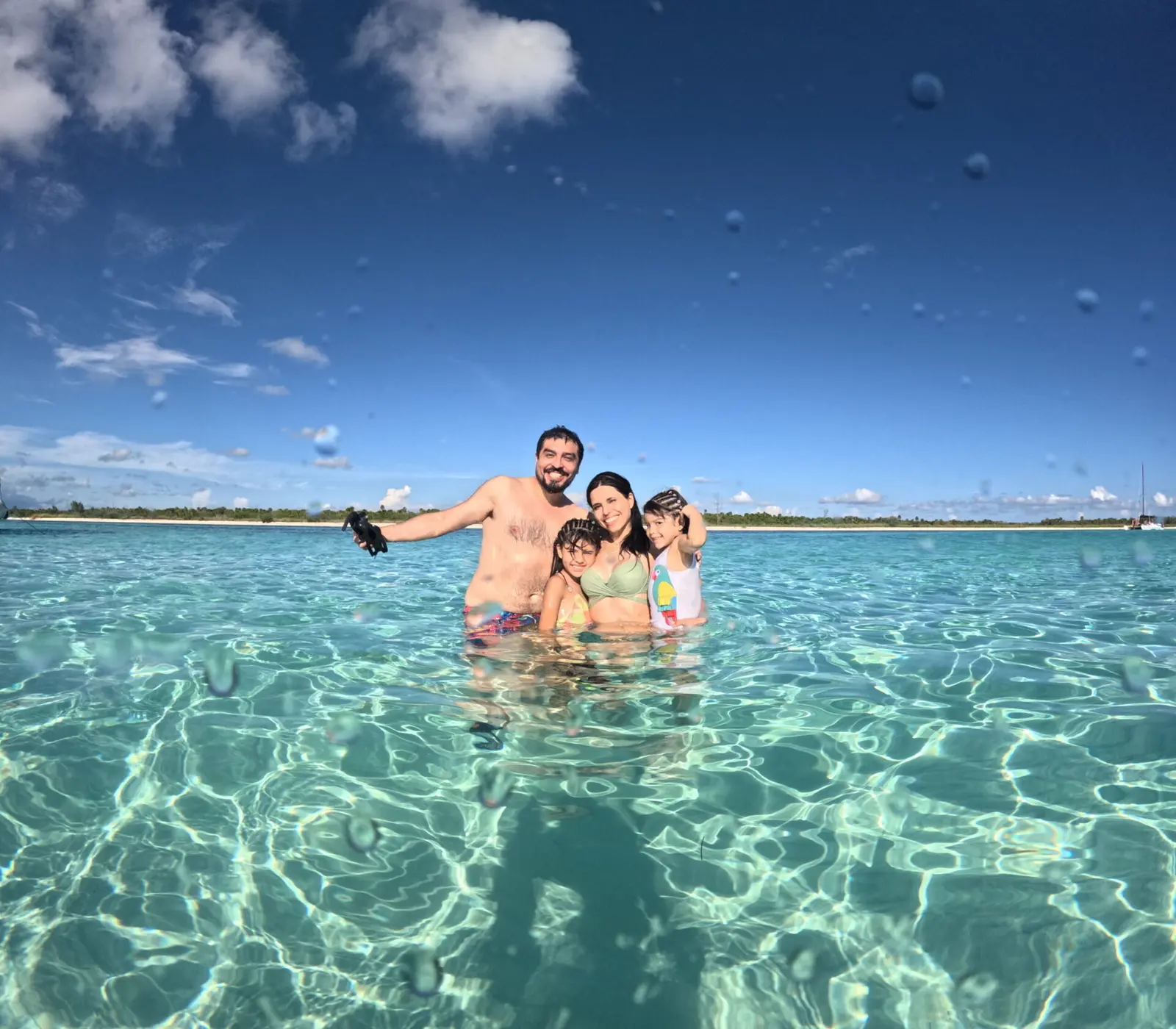 Family taking a selfie while standing in clear, shallow turquoise water off Cancún