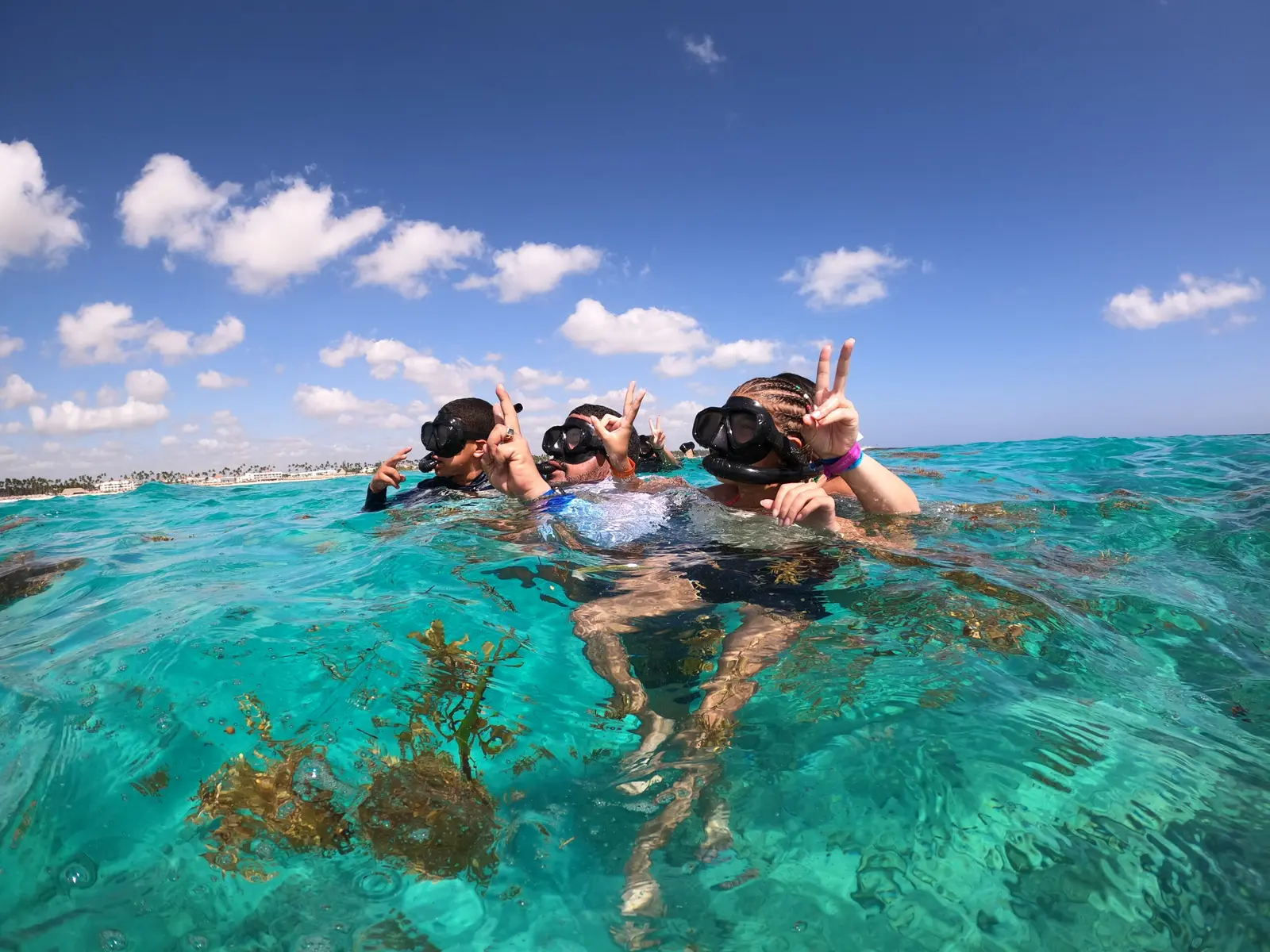 Three snorkelers flashing peace signs at the surface of clear turquoise water