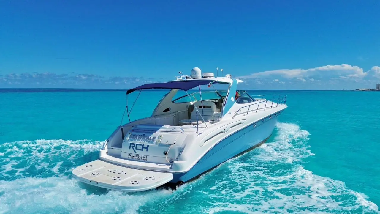 Motor yacht pulling away with a white wake across turquoise water toward the Cancún shoreline