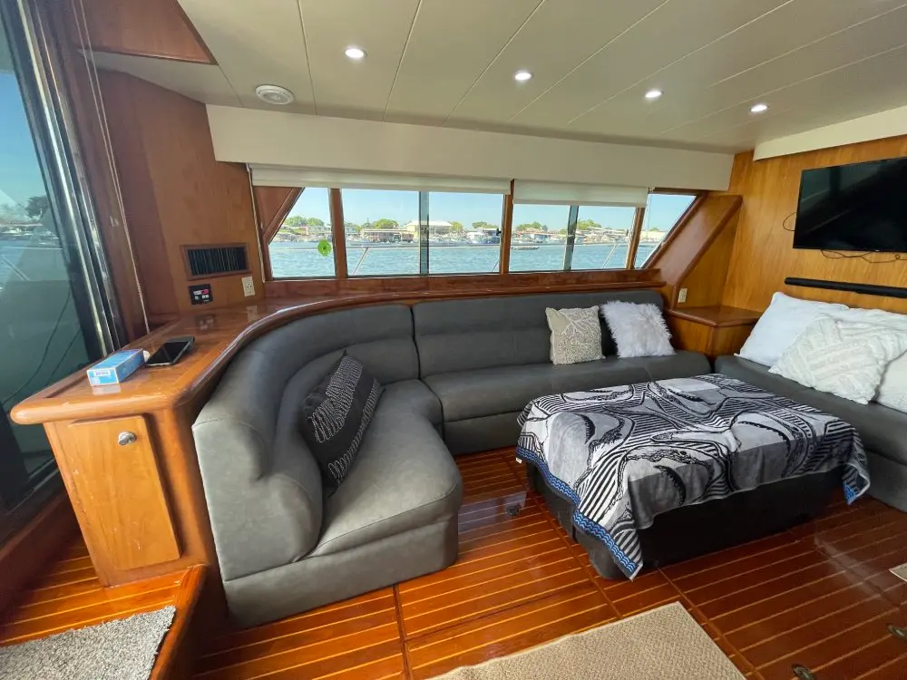 Yacht saloon with a gray sectional sofa, a made-up double bed, teak floors and a wall-mounted TV