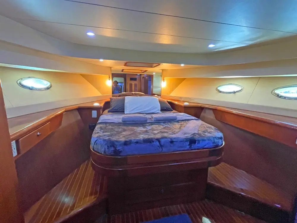 Master cabin on the yacht with a blue-covered double bed framed by portholes and wood paneling