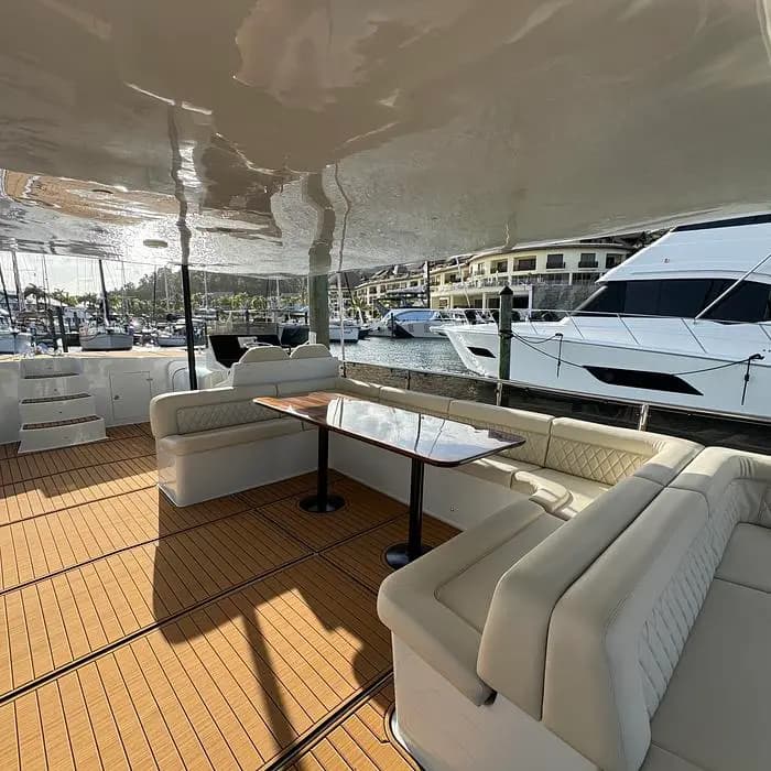 U-shaped cream sofa around a dark table under the power catamaran's hardtop, a motor yacht docked alongside
