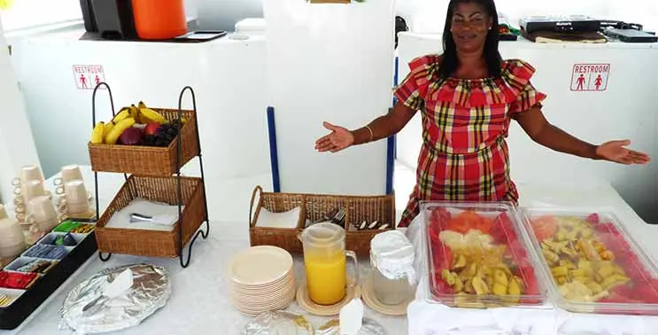 A woman in a plaid dress presenting fruit platters, snacks and juice aboard the catamaran