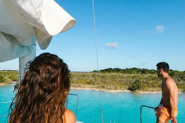 Two guests at the bow of a sailing catamaran looking toward a mangrove shore on the lagoon