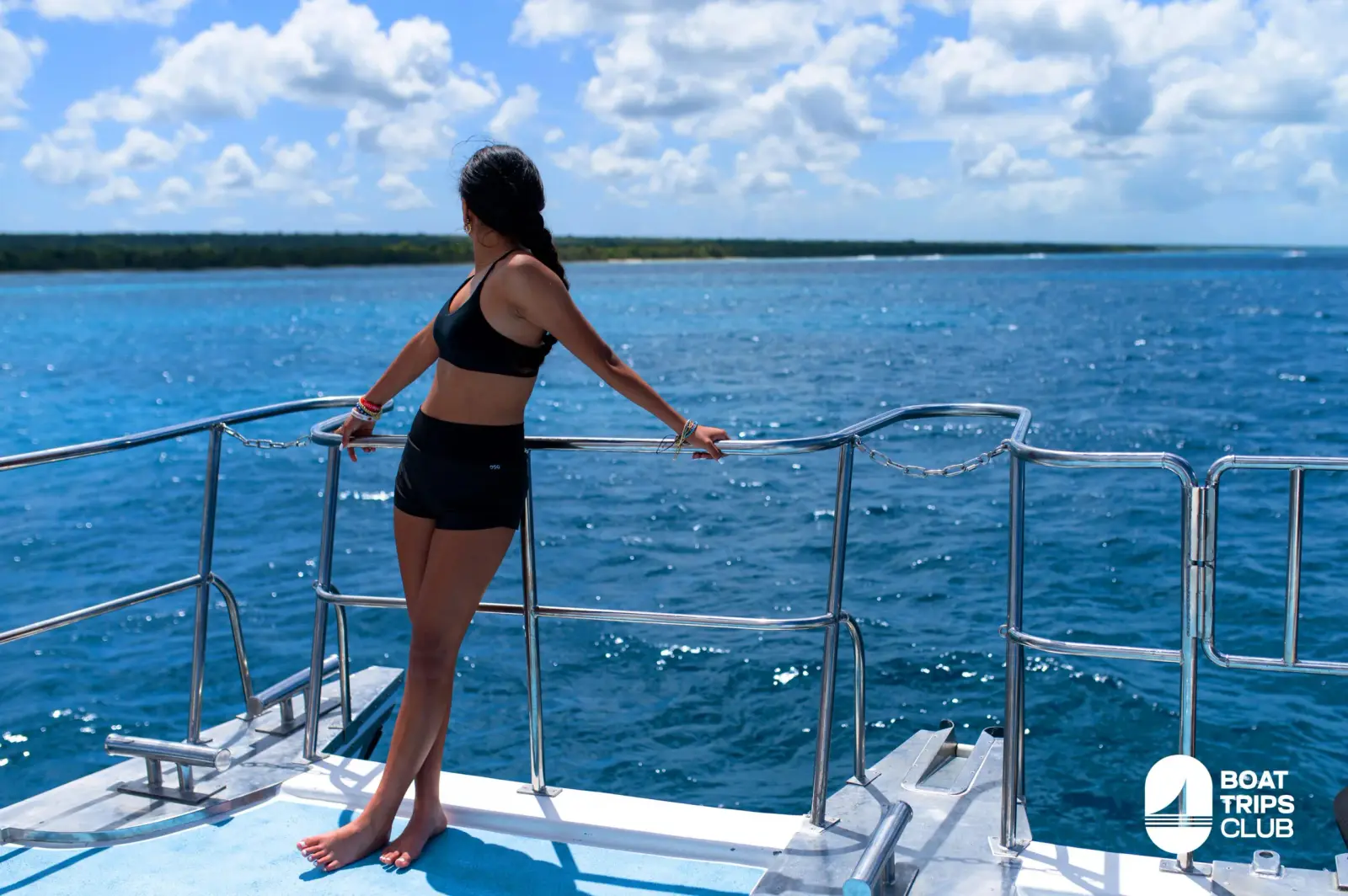 Woman in black swimwear at the catamaran rail gazing out at the deep blue sea and Bayahibe coastline