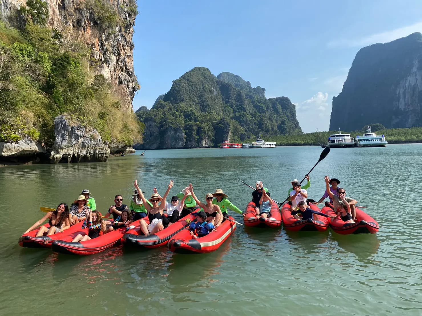 Guests cheering and raising paddles from red sea canoes among the limestone karsts of Phang Nga Bay