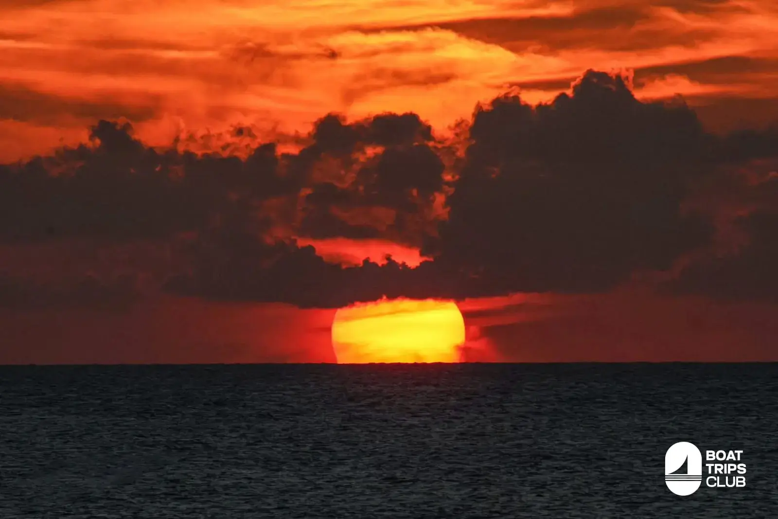 Red sun sinking into the sea off Punta Cana beneath a band of dark clouds