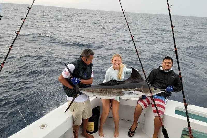 A woman and two men holding a marlin at the stern of a sportfishing yacht among trolling rods