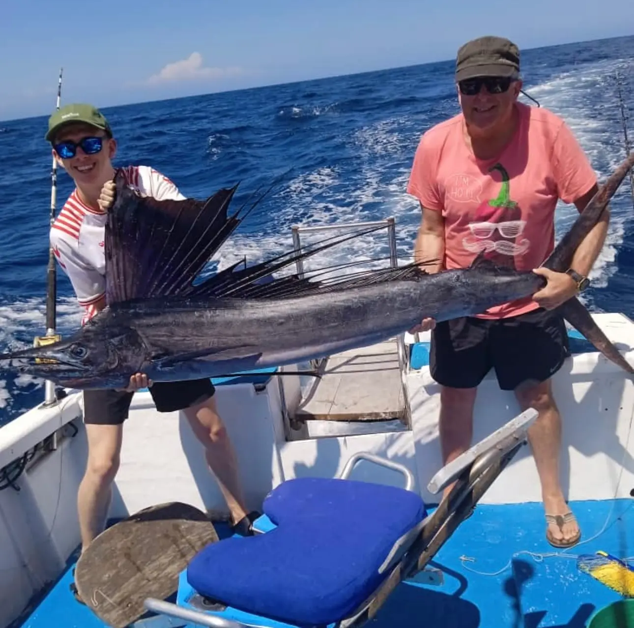 Two anglers holding up a sailfish across the deck of a center console boat on the open Pacific