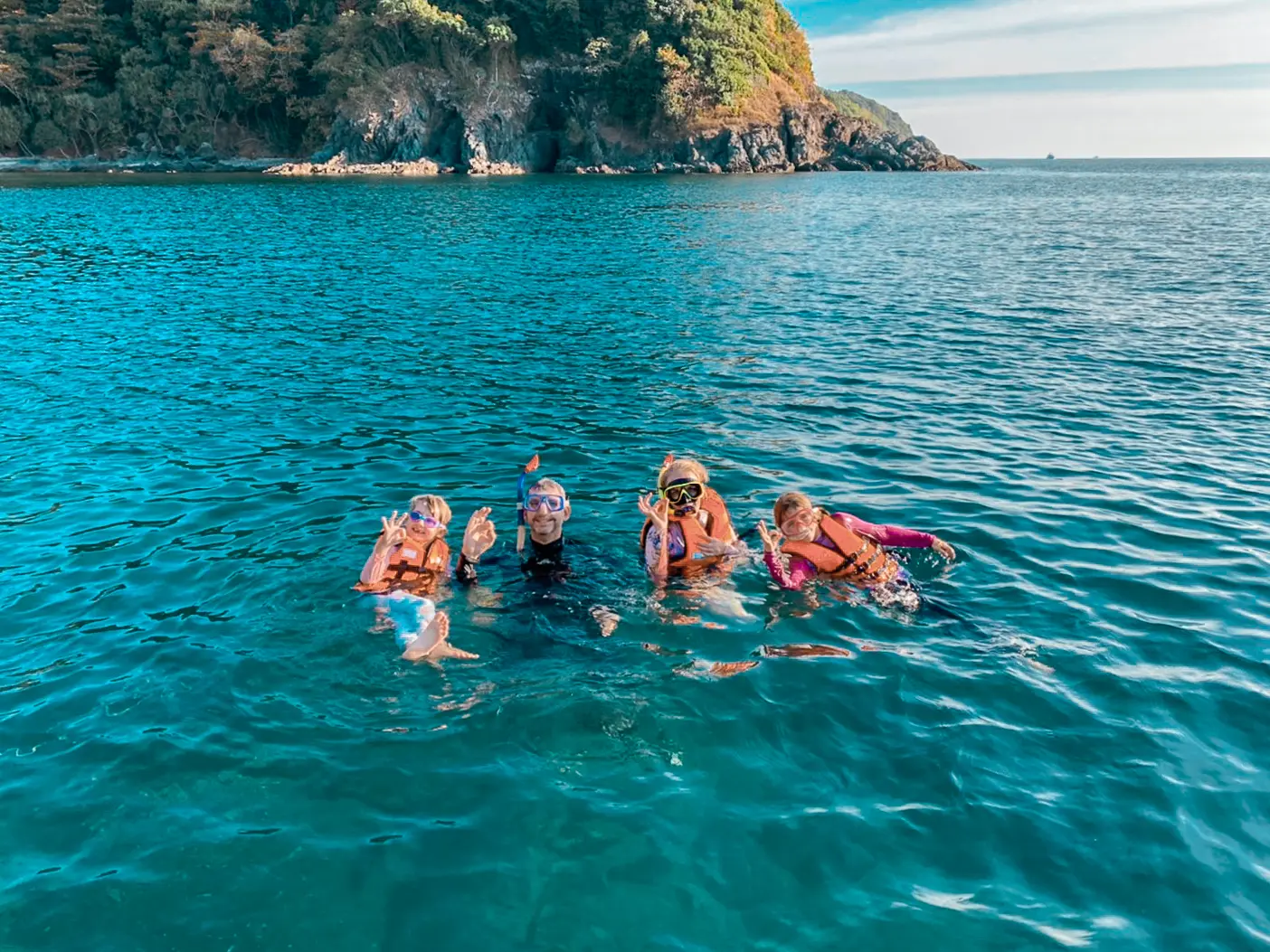 Four snorkelers in life vests floating together in clear blue water off a rocky island south of Phuket