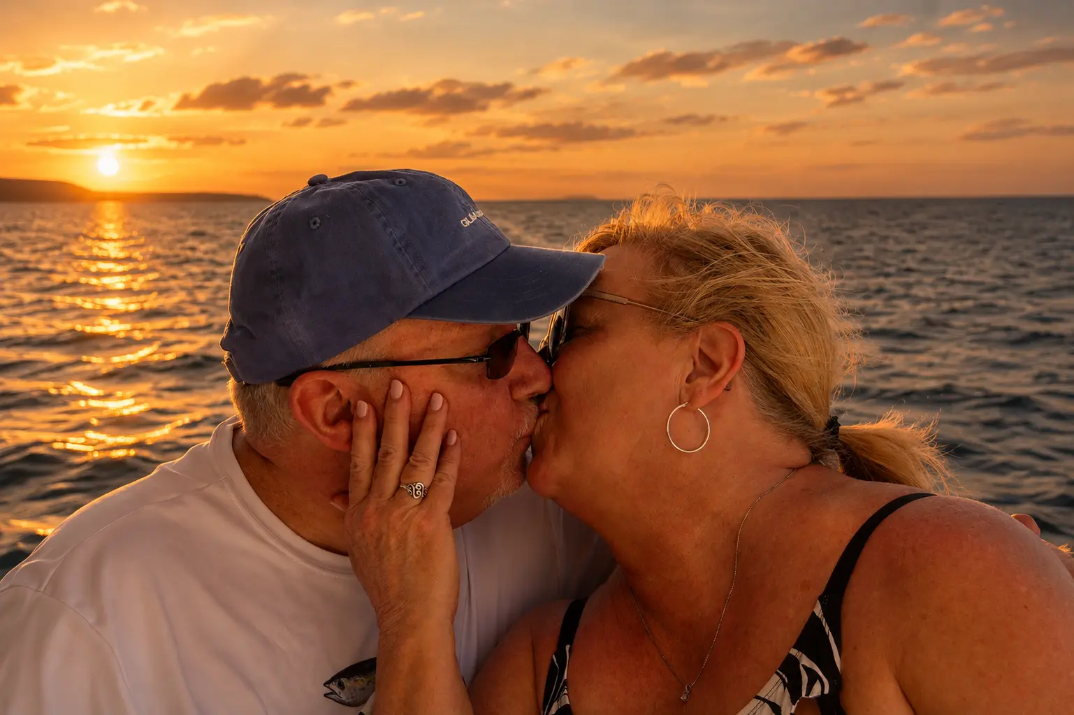 Couple sharing a kiss on deck, the sun setting over the sea behind them