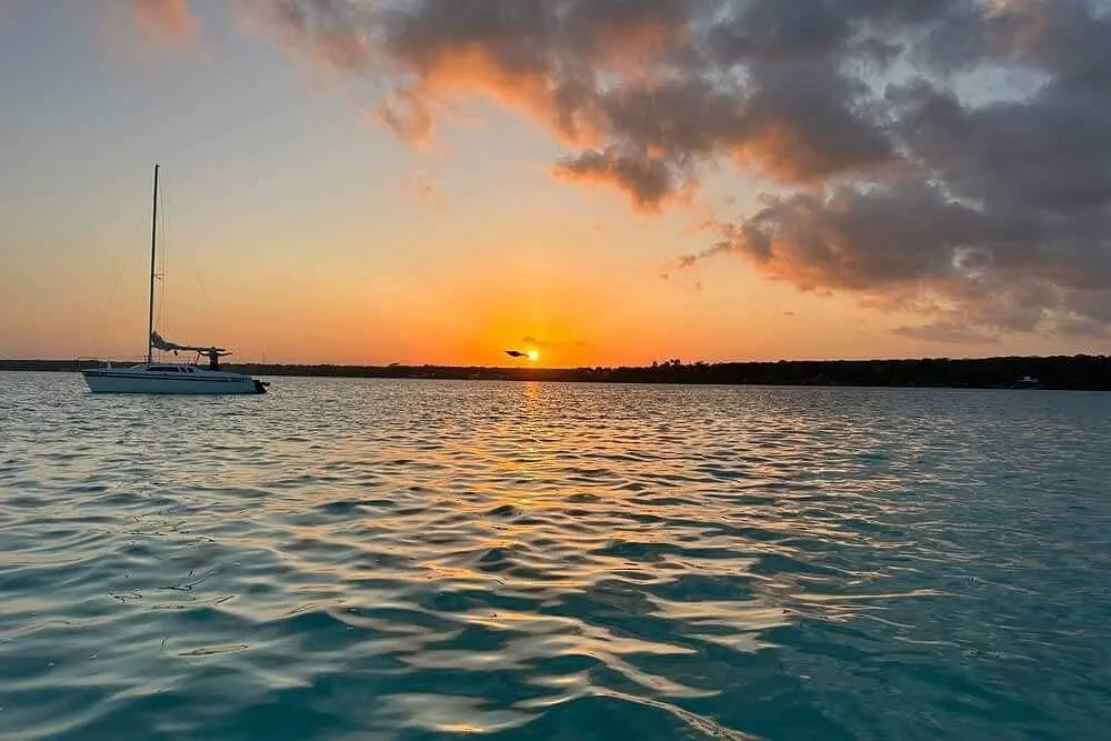 Low sun glowing over Bacalar Lagoon with a sailboat silhouetted at anchor
