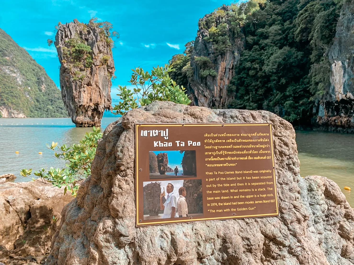 Bronze information plaque on a rock at James Bond Island, the needle rock rising from the water behind