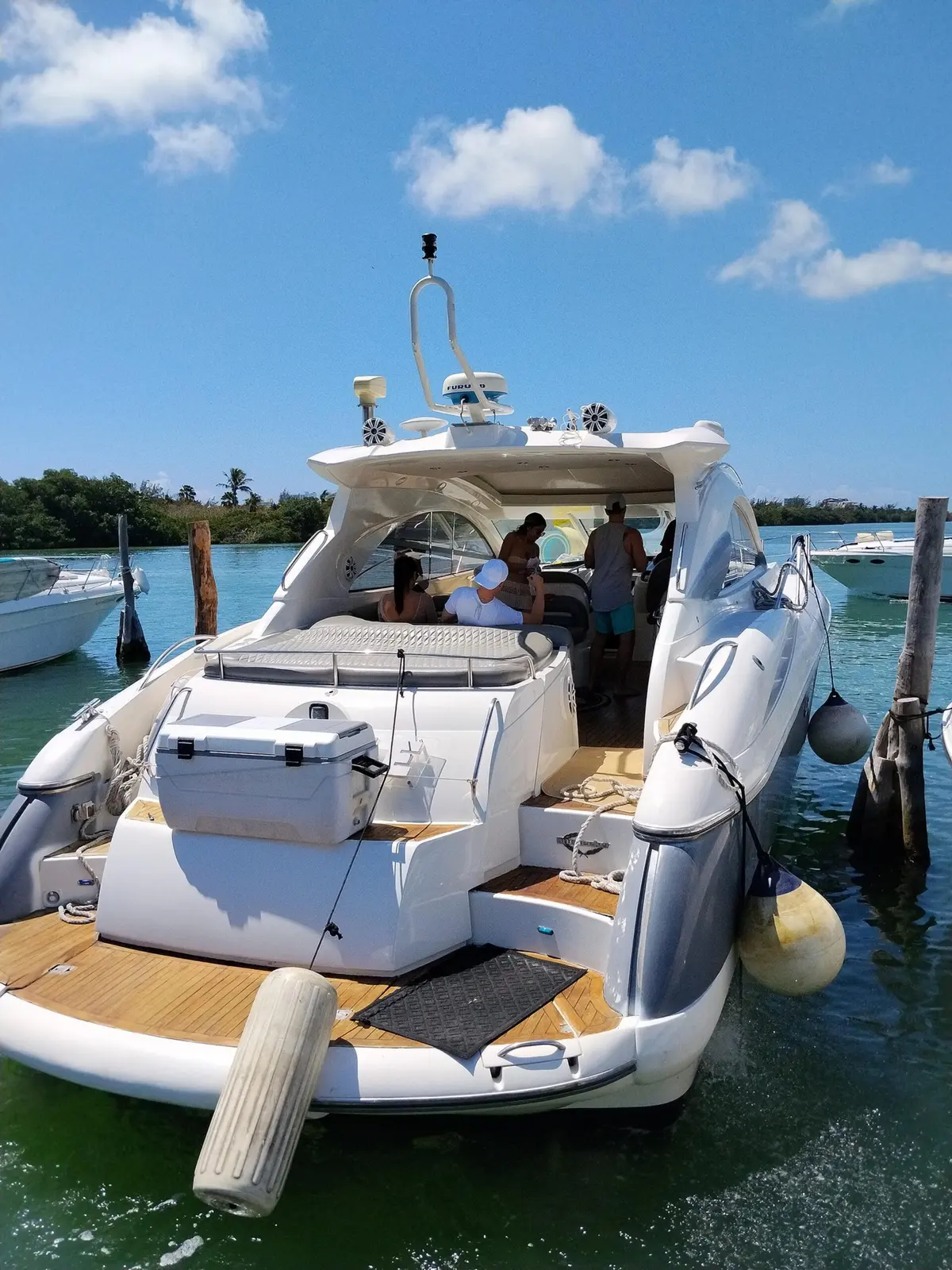 Stern and swim platform of a motor yacht moored at a mangrove-lined marina with guests aboard