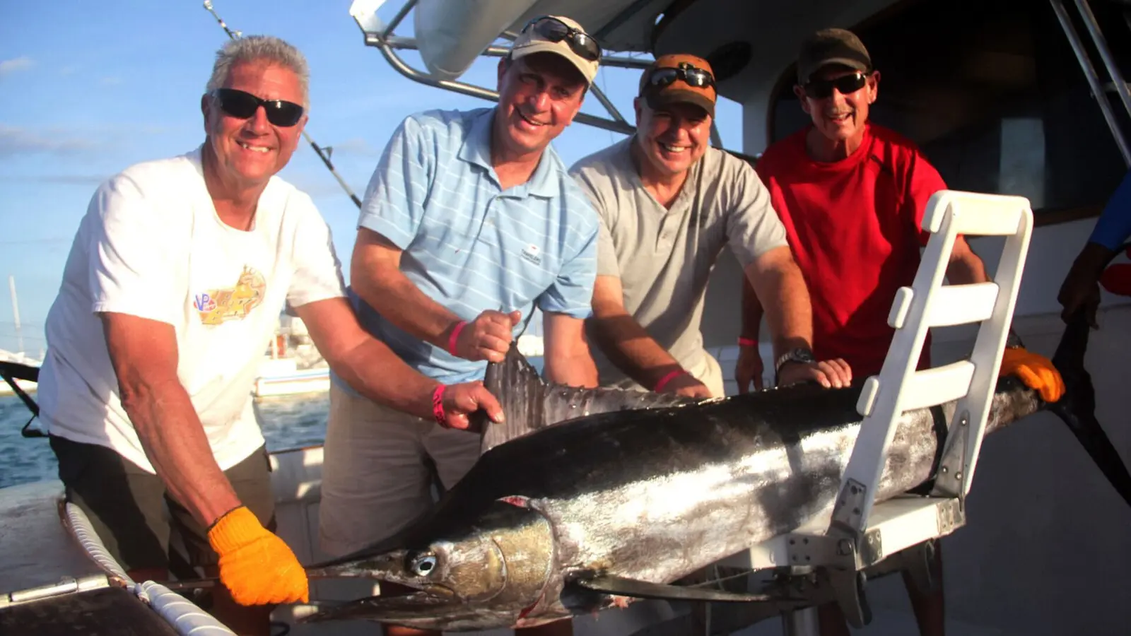 Four anglers posing with a large billfish beside the flybridge ladder of a sportfishing boat