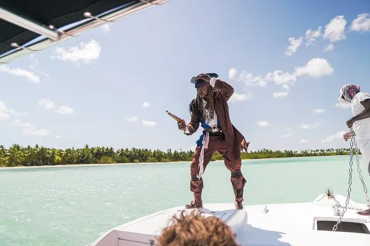 A man in a pirate costume posing on a catamaran bow above shallow turquoise water near palms