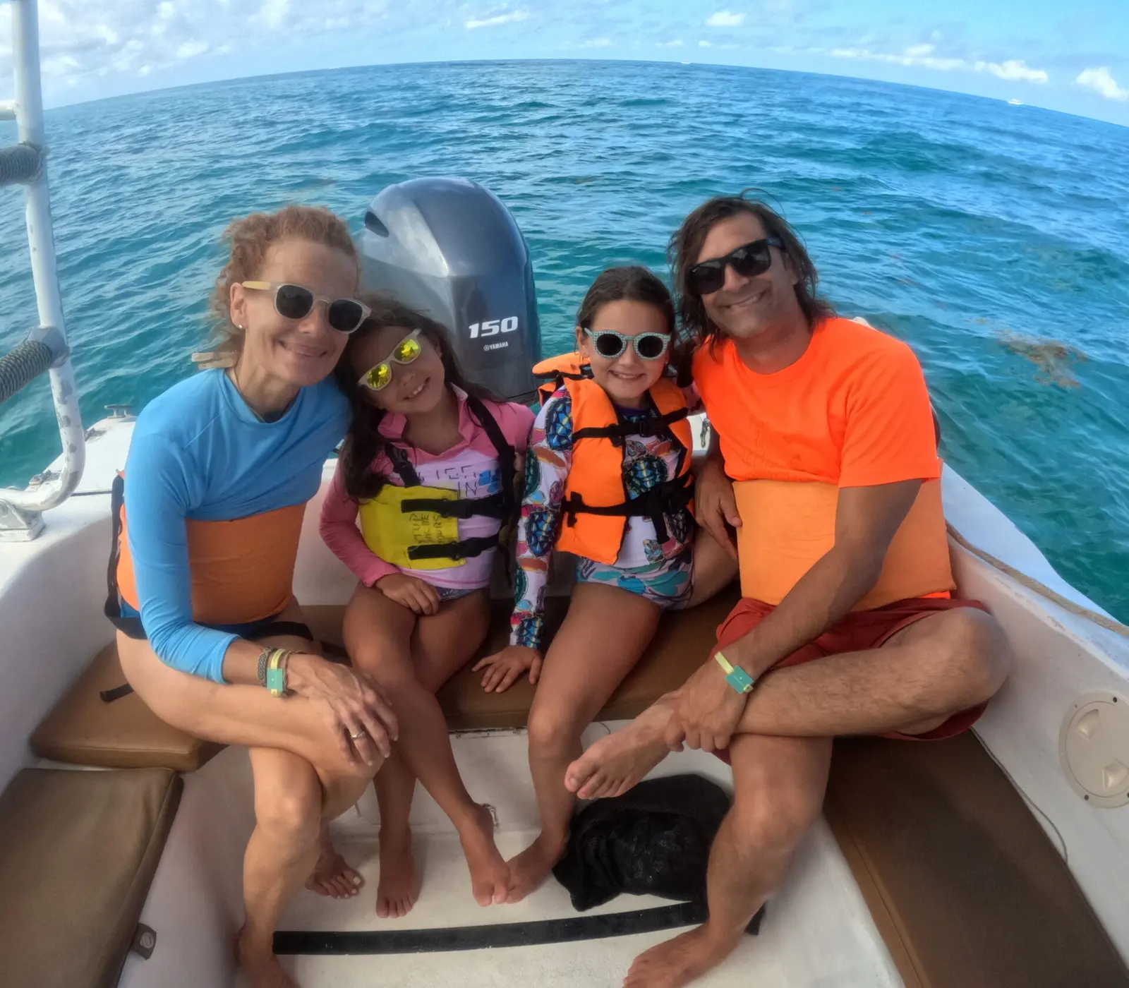 Family with two girls in life vests posing at the speedboat's stern by the outboard motor