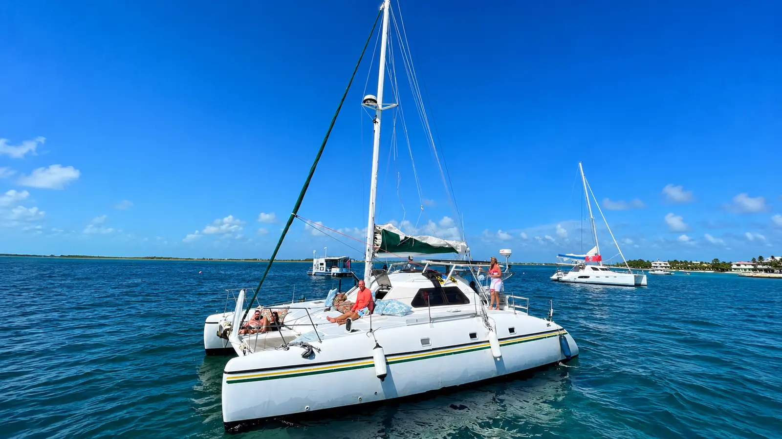 Guests lounging aboard a sailing catamaran anchored in deep blue water off Belize, another catamaran nearby