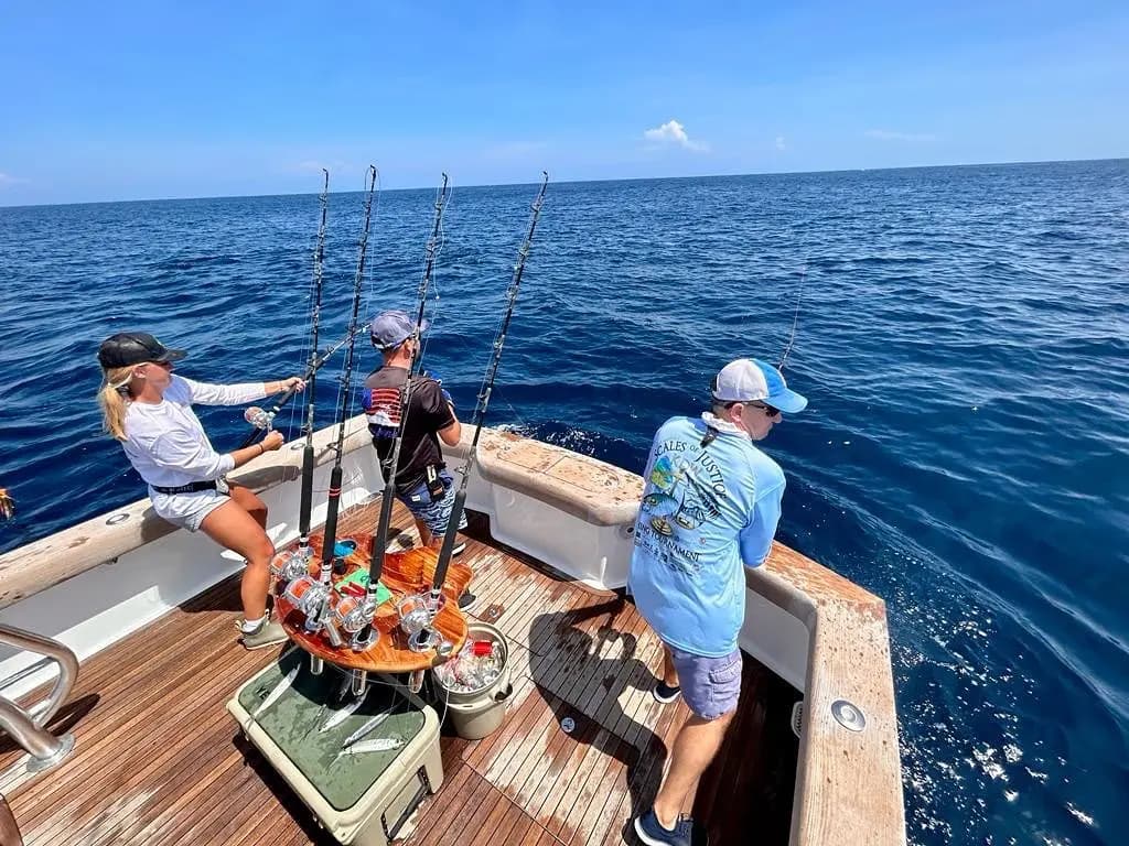 Three anglers on the teak cockpit of the sportfishing boat watch their lines on the open Pacific
