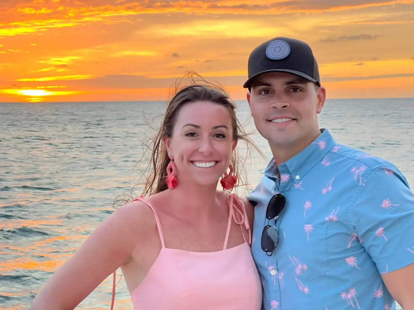 Couple smiling together as the orange sun sets over the sea behind them