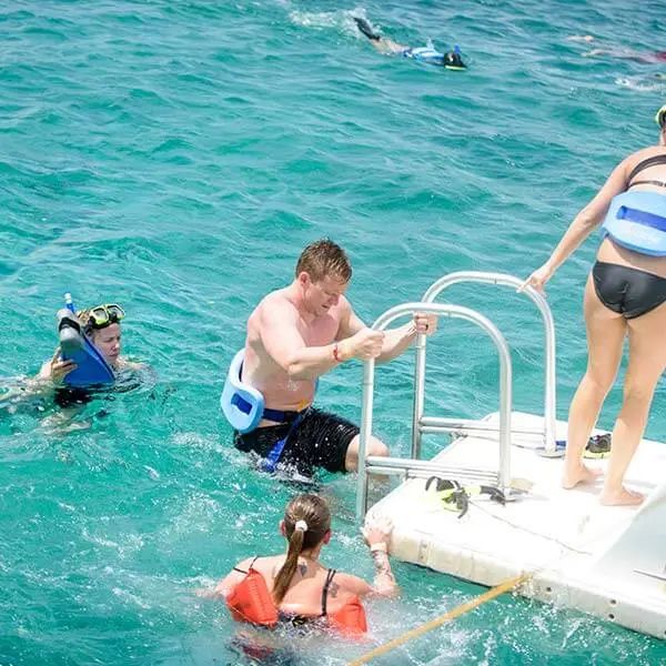 A man climbing the swim ladder back onto a catamaran as others snorkel nearby