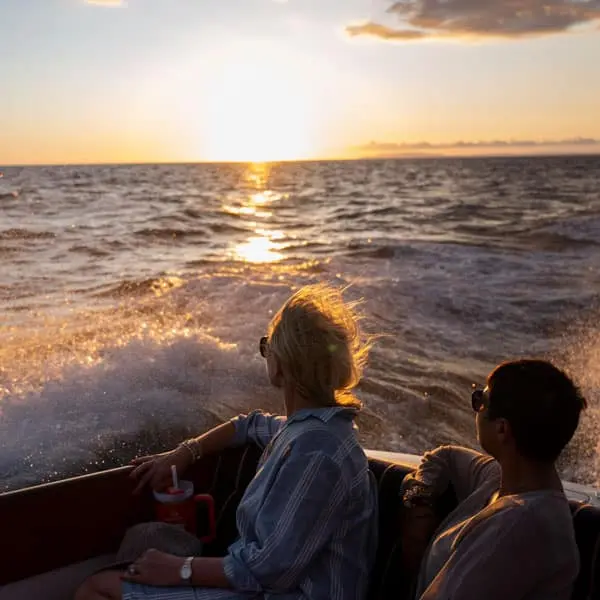 Couple seated at the boat's stern watching the sunset across the spray of the wake