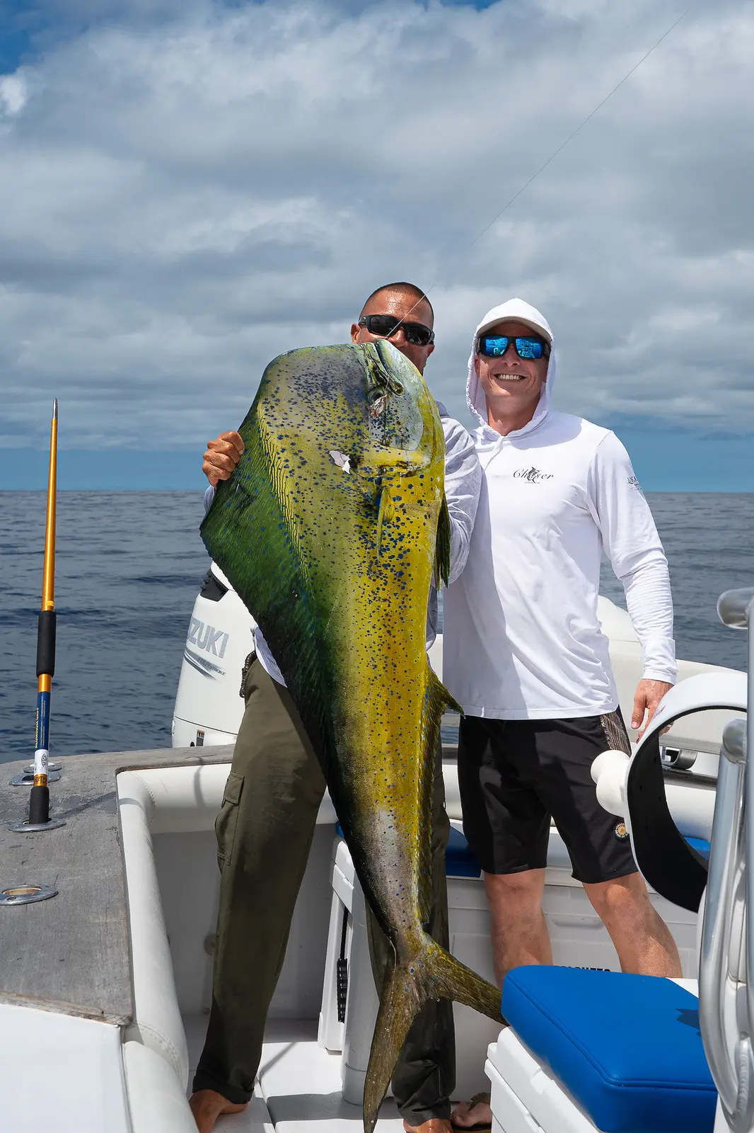 Crew member and angler posing on a center-console boat with a large mahi-mahi held upright